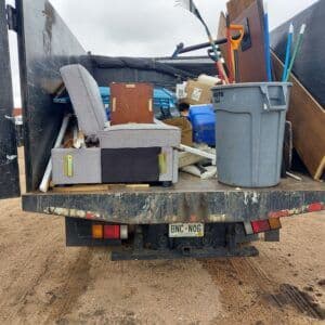 Truck bed filled with furniture, debris, and recycling materials ready for disposal.