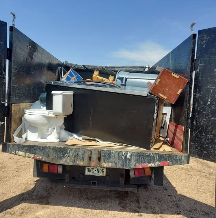 Truck bed filled with various discarded appliances and furniture ready for disposal.