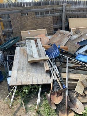 Piled debris including wood, tools, and other materials in a cluttered yard.