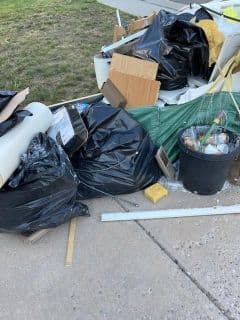 Black garbage bags and debris scattered on the ground, including wood and a plant pot.