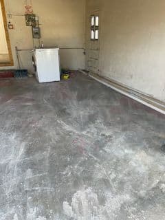 Empty garage with dirty concrete floor, washing machine, and bare walls.