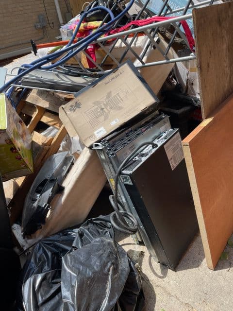 Cluttered pile of discarded furniture, appliances, and miscellaneous items in an outdoor area.