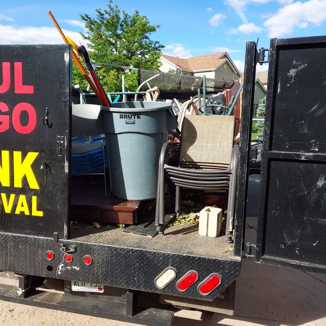 Truck filled with various items for junk removal, including furniture and trash bins.