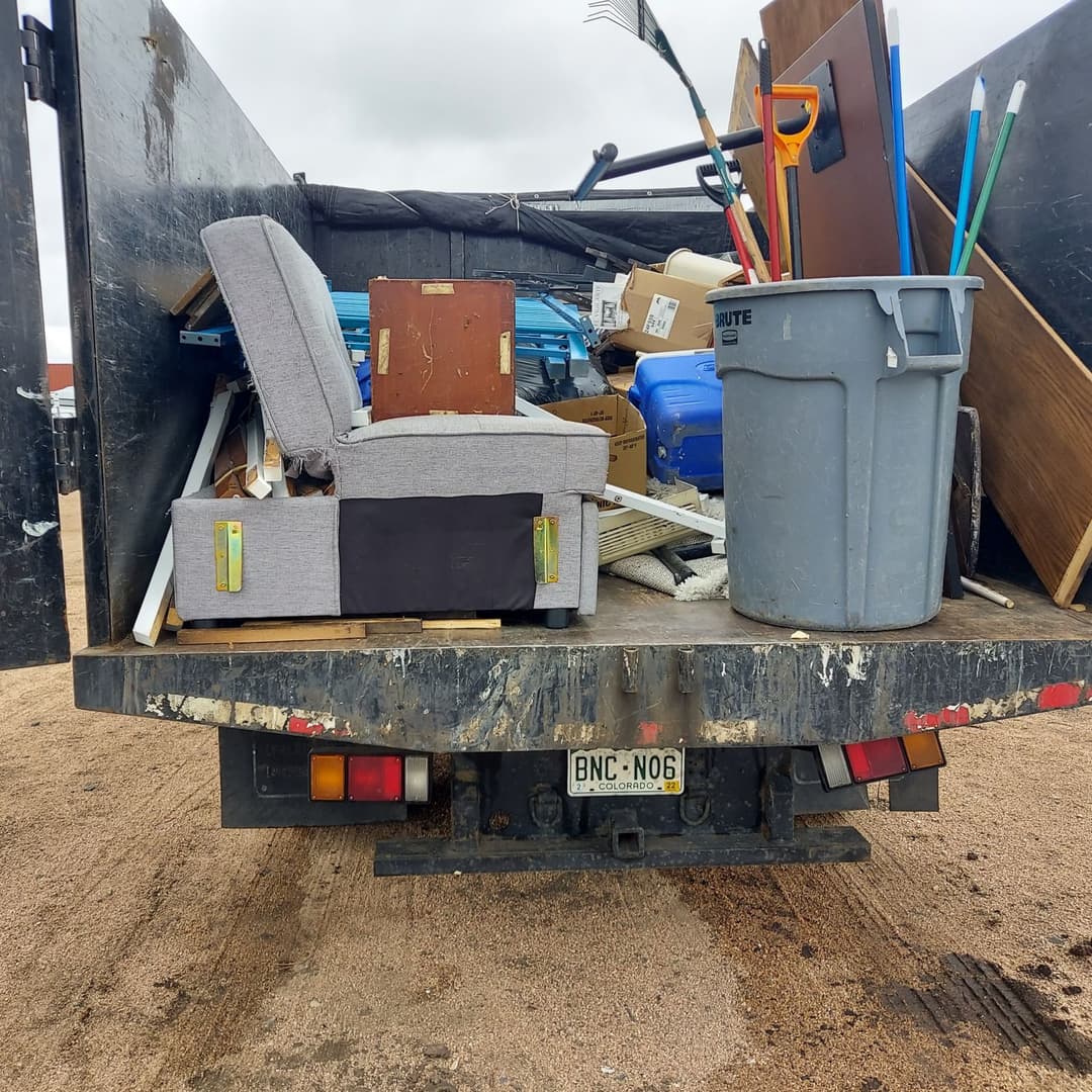 A truck bed filled with various items including furniture, boxes, and cleaning supplies.