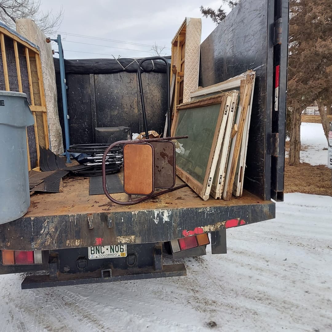 Truck bed filled with discarded furniture and debris, including frames and a metal table.